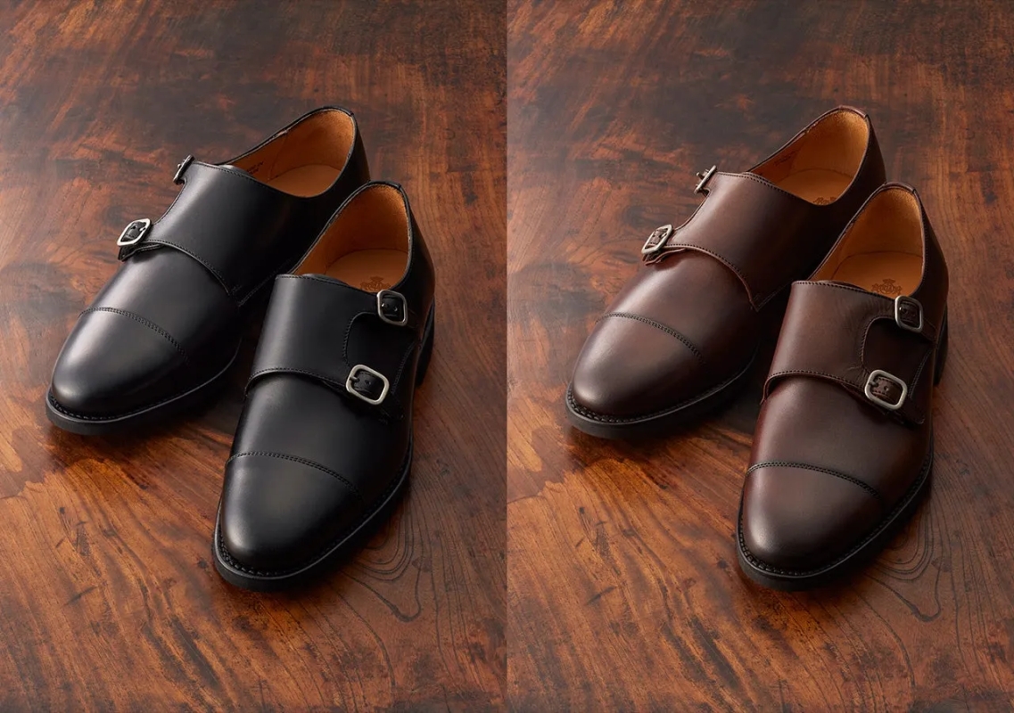 2足の革靴が並べられた写真です。左側には黒色のダブルモンクストラップシューズ、右側には茶色のダブルモンクストラップシューズが写っています。どちらの靴も木製のテーブルの上に置かれています。