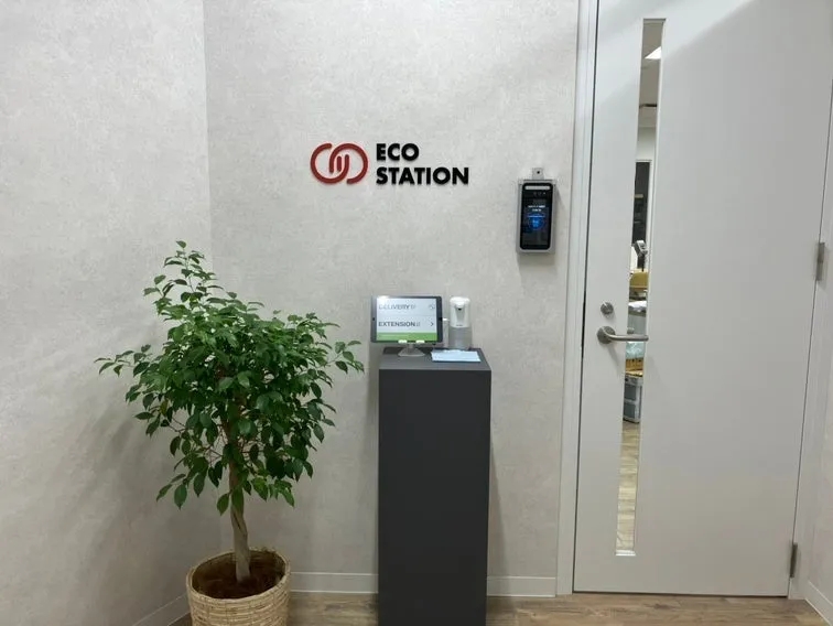 入り口の様子。ECO STATIONと書かれたロゴがあり、顔認証システム、タブレット、観葉植物、ドアが見える。