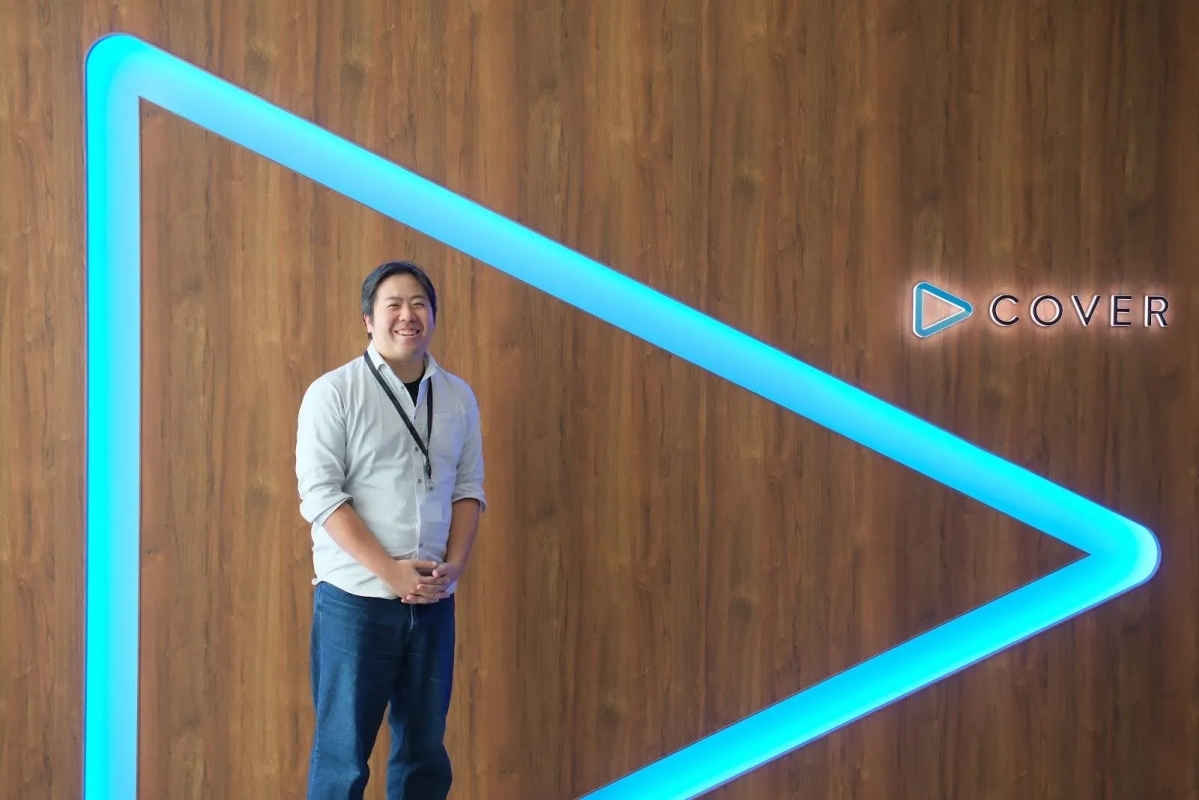 木目調の壁の前に立つ男性の画像