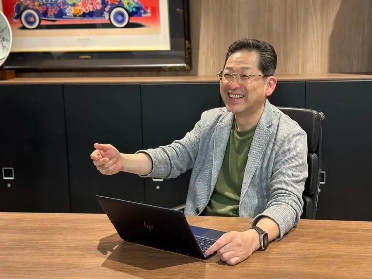 笑顔の男性がノートパソコンの前に座り、話をしている様子。