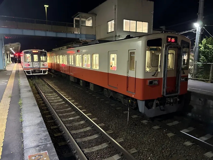 夜の駅に停車中の電車。2つの電車が並んでおり、駅のホームの照明が灯っている。