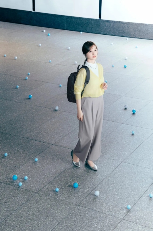 女性がカーディガン、パンツ、リュックサックを身につけ、青いボールを見つめる着用イメージ