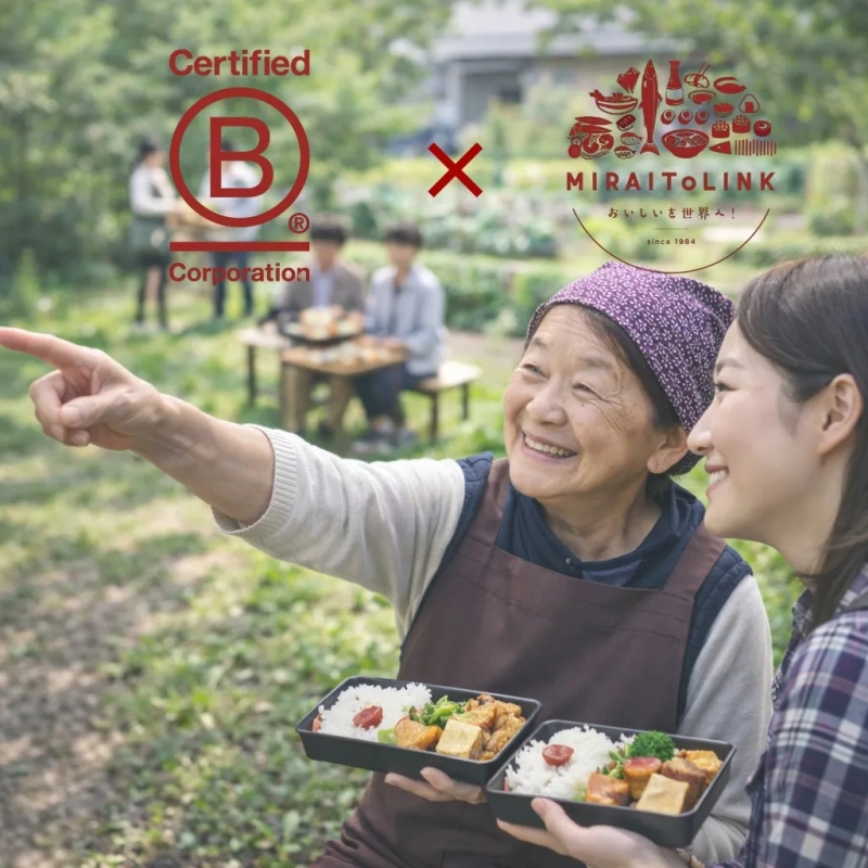 二人の女性が弁当を持って外で食事を楽しんでいる写真。年配の女性が指を指し、若い女性が笑顔でそれを見ている。背景には、他の人々がテーブルを囲んでいる様子が写っている。弁当には、ご飯、おかず、梅干しが入っている。