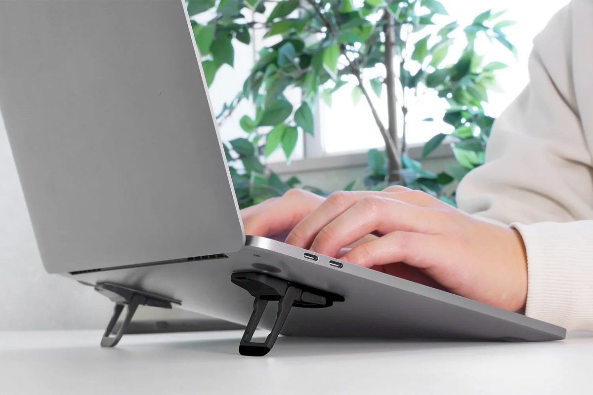 ノートパソコンを使用している様子。ノートパソコンはスタンドで持ち上げられており、人がキーボードを叩いている。