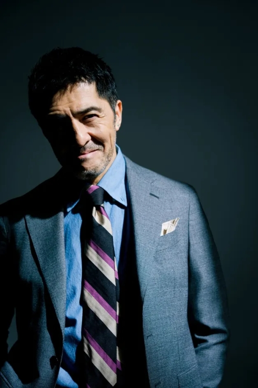 スーツを着た男性のポートレート。男性は微笑んでおり、顔の一部は影になっている。ネクタイはストライプ柄。